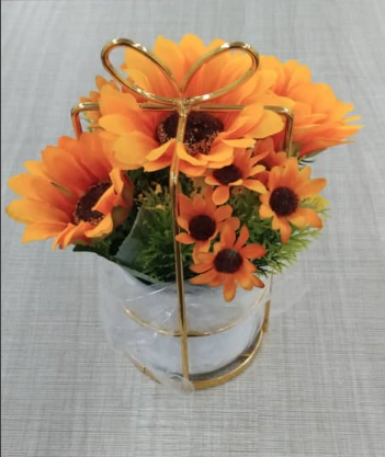 Decorative arrangement of sunflowers in a clear vase with a gold bow on a gray background